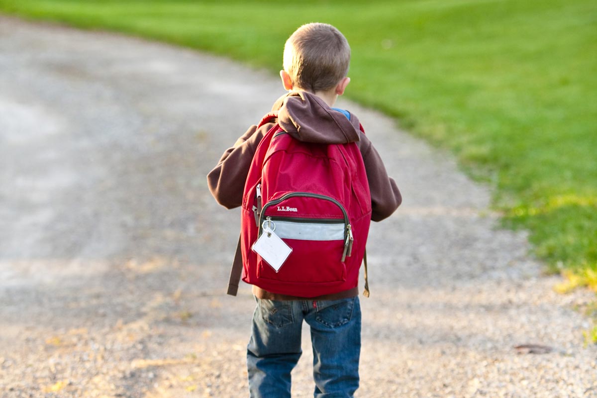 An elementary school boy walking towards school wearing a big red backpack