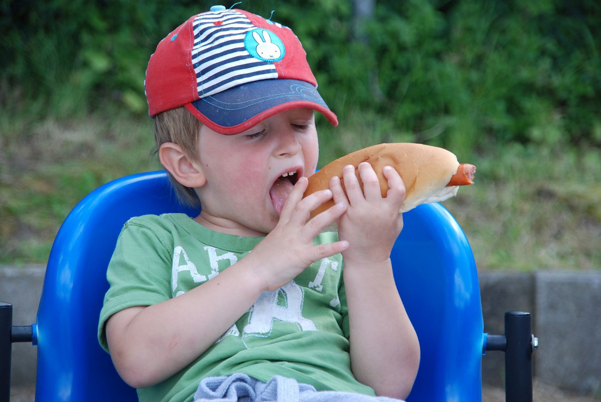 A young boy in a baseball cap eating a hot dog