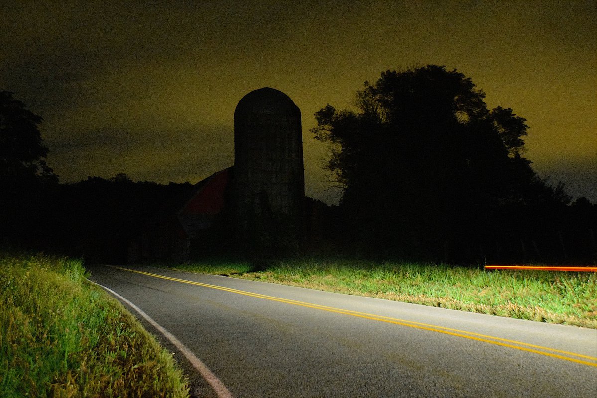 Car headlights cut through the darkness of a rural farm area