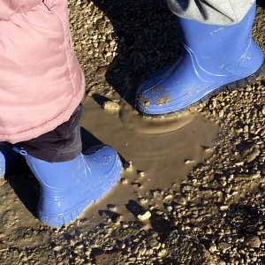 Two kids playing in a mud puddle in blue gumboots