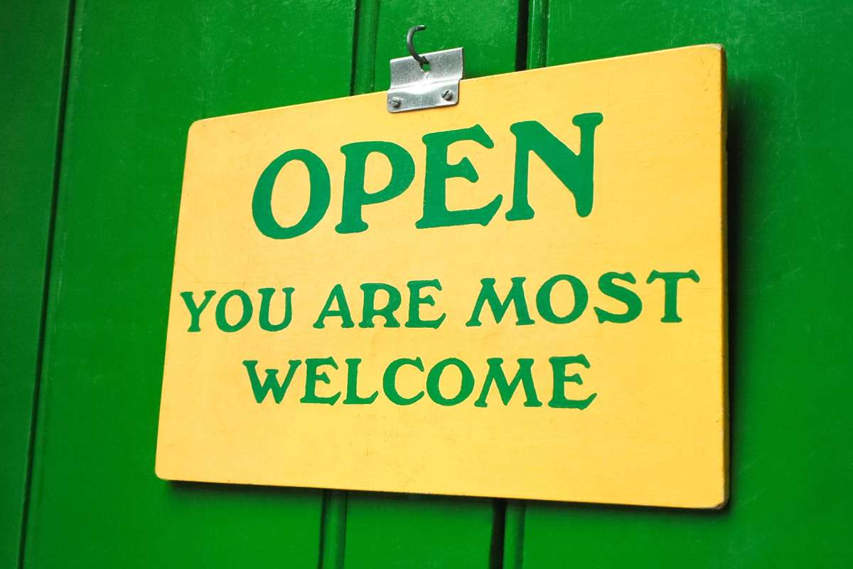 Yellow sign with green lettering that says: Open, You Are Most Welcome